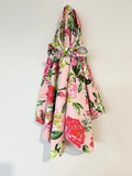 A pink floral jersey baby wrap with a matching headband featuring large red and pink flowers and green leaves, hanging against a plain off-white wall.