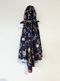 A navy blue fabric jersey baby receiving wrap and headband with a floral vine pattern in orange, white, and light blue, tied at the top and hanging against a plain off-white wall.