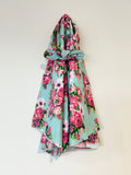 A light mint green baby wrap in jersey and a headband with a vibrant pink and green floral print, tied in a knot at the waist and draped down, shown against a plain off-white background.