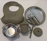 A 6-piece baby feeding set in a muted olive green color, including a silicone bib, a divided plate with utensils, a stainless steel bowl, a ribbed sippy cup, a small spoon, and a lid, arranged on a white background.