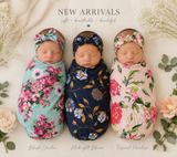 Three newborn babies are shown sleeping and swaddled in floral wrap blankets with matching headbands, arranged on a soft cream fabric with decorative flowers and leaves. Text at the top reads “NEW ARRIVALS” and labels the three colors/styles as “Blush Garden,” “Midnight Bloom,” and “Tropical Paradise.