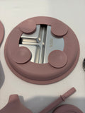 A close-up of a pink silicone suction cup lid with a stainless steel center insert, featuring the text 'SUS304' and small circular icons. Other matching silicone parts are partially visible on a white surface.