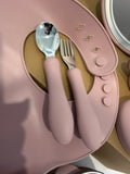 Pink silicone baby spoon and fork set with metallic silver handles, displayed on a matching pink silicone feeding tray.