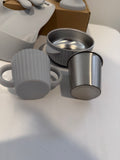 Gray silicone baby feeding accessories including a ribbed handled cup and a stainless steel bowl, shown with a cardboard box on a white surface.