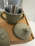 Sippy cup top silicone in an olive sage green with cups with handles on a brown box 