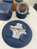 A close-up of a blue silicone baby feeding tray with suction cups and a stainless steel insert, with other matching blue baby feeding accessories in the background on a white surface.