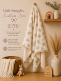 A cream-colored muslin baby wrap with a delicate floral pattern and scalloped edges, hanging on a wooden peg on a warm beige wall. The scene is styled with a wicker basket, a small plush bunny, a ceramic vase with dried grass, and a wooden sign that reads 'NEW ARRIVAL'.
