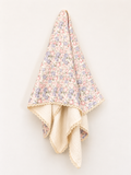 A folded quilted blanket with a delicate pastel floral print on one side and a soft cream-colored textured reverse side, finished with scalloped lace trim, shown against a plain off-white background.