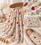 A collage showing a baby blanket and matching swaddle with a colorful fruit print. The left panel shows the blanket draped over a wicker basket in a nursery setting with a stuffed bunny.